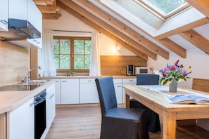A kitchen with a skylight, wooden beams, a dining area with a table and chair, and a window with curtains. - 'Lotschenhof Apartment Margerite' with Mountain View, Garden & Wi-Fi (Trodena)