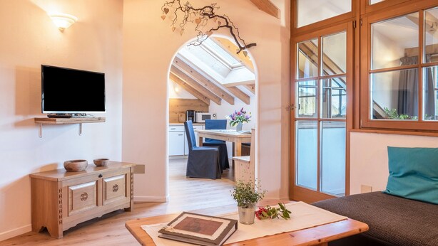 Un salon chaleureux avec un téléviseur, des meubles en bois, un coin repas et, à travers une arche, une vue sur la cuisine.