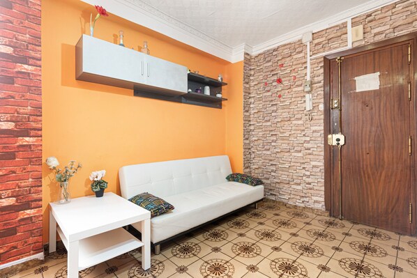 Una habitación con un sofá blanco, una mesita con un florero, una pared de ladrillo, una pared de piedra y una puerta de madera.