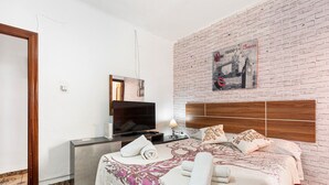 A hotel room with a brick wall, a bed with a floral bedspread, a TV on a stand, and a poster of London.