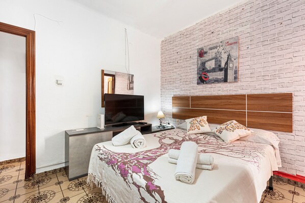 A hotel room with a brick wall, a bed with a floral bedspread, a TV on a stand, and a poster of London.