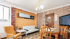 A living room with a sofa, dining table, chairs, a TV, and a brick wall.