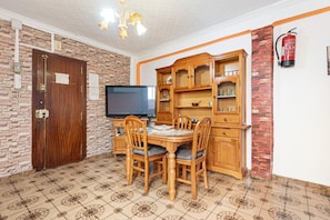 Un coin repas avec une table et des chaises en bois, un téléviseur et un mur décoré d’un motif en briques.