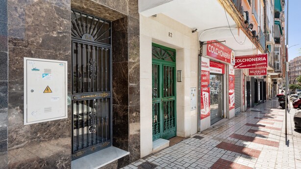 A building facade with numbered doors, a sign for a furniture store, and a utility box with a warning label.