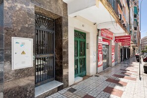 Fachada de edificio con puertas numeradas, un letrero para una tienda de muebles y un cuadro de electricidad con etiqueta de advertencia.