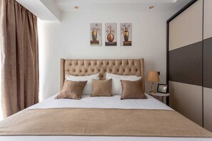 A neatly made bed with a tufted headboard, a bedside table with a lamp, and three framed artworks on the wall.