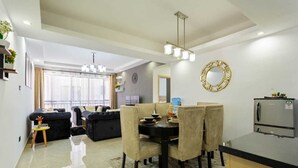 A modern living room with a dining area, a sofa, a chandelier, and a refrigerator. - Stay.Plus Splash of Glam Lavington (Nairobi)
