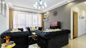A modern living room with two black sofas, a TV, and a chandelier. - Stay.Plus Splash of Glam Lavington (Nairobi)