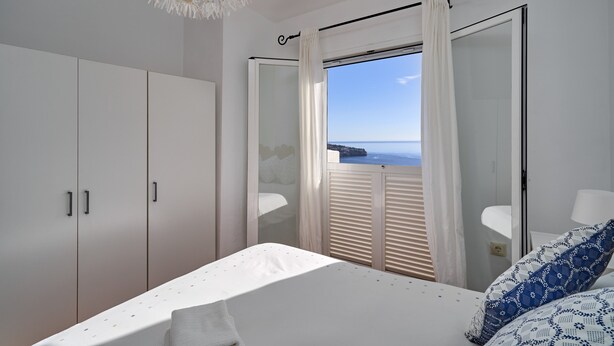 Ein Schlafzimmer mit Bett, Kleiderschrank, Fenster mit Vorhängen und Meerblick.