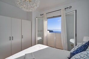 Un dormitori amb un llit, un armari, una finestra amb cortines i vista al mar.