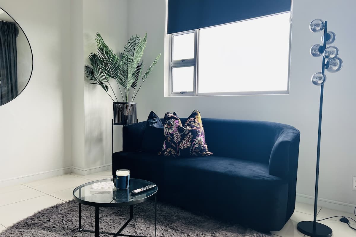 A modern living room with a blue sofa, a glass coffee table, a potted plant, and a floor lamp.