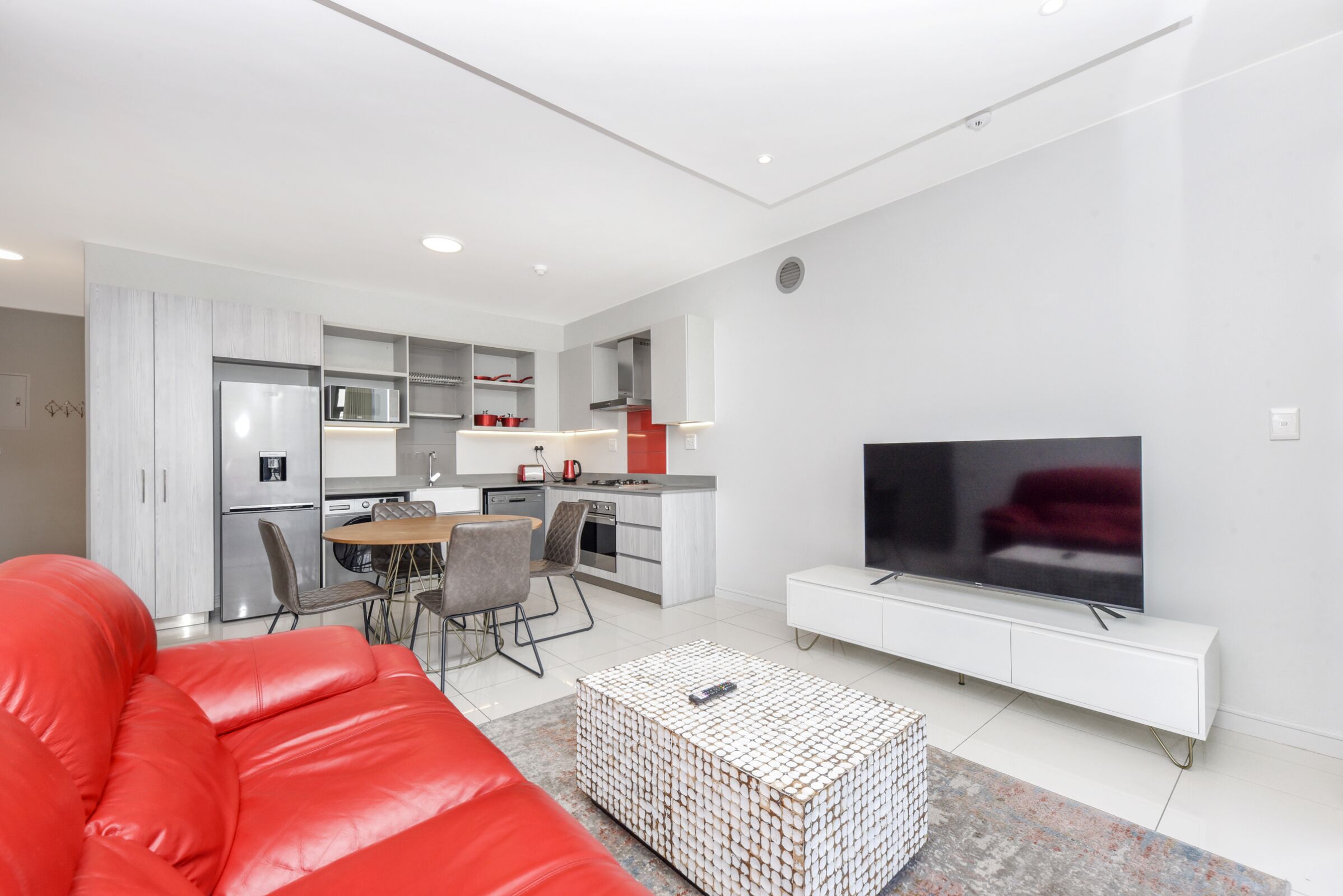 Un salon moderne avec un canapé rouge, une table basse et un téléviseur posé sur un meuble blanc.