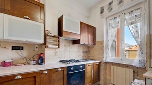 A kitchen with wooden cabinets, a gas stove, a built-in oven, and a window with curtains. - Apartment "A due passi dal mare" with Mountain View, Balcony & Wi-Fi (Pietra Ligure)