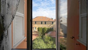 A view through a window with shutters, a building with a red roof, and a tree in the foreground. - Apartment "A due passi dal mare" with Mountain View, Balcony & Wi-Fi (Pietra Ligure)
