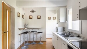 Une cuisine avec des meubles blancs, un évier, une cuisinière et trois tabourets.