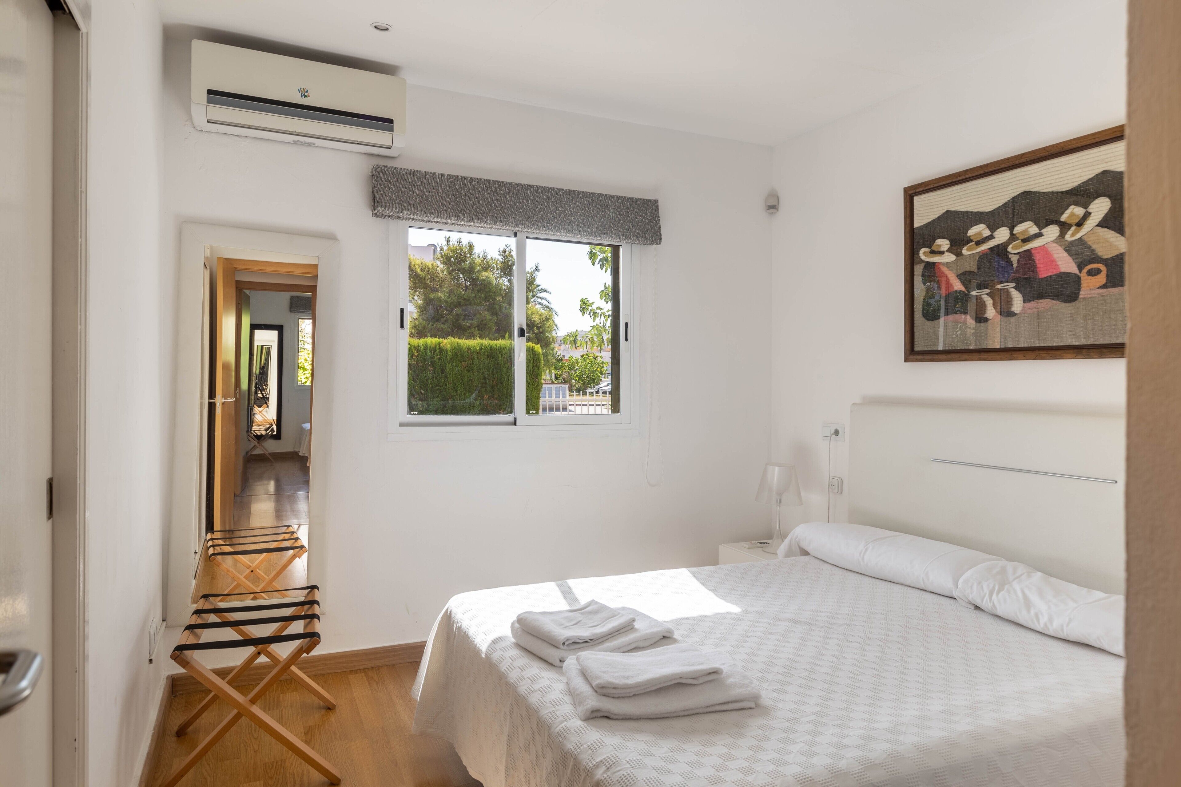 Une chambre avec un lit, une fenêtre donnant sur un paysage agréable, une porte menant à une autre pièce et un climatiseur fixé au mur.
