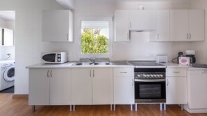 Une cuisine moderne avec des meubles blancs, un four à micro-ondes, une cuisinière, un lave-vaisselle et une fenêtre donnant sur un paysage verdoyant.