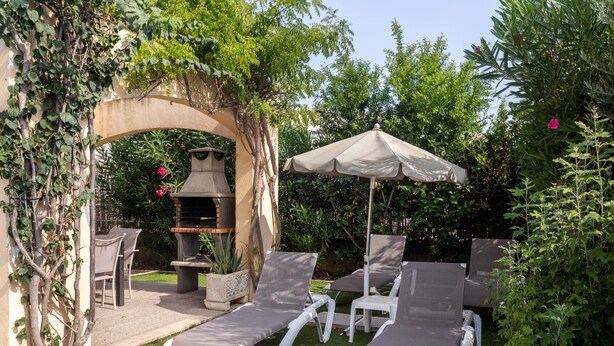 Une terrasse avec des chaises longues, un barbecue et une pergola recouverte de plantes grimpantes.