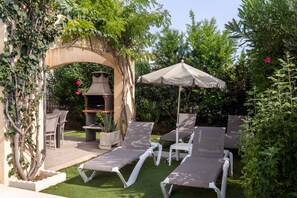 Un patio con sillones de descanso, una parrilla y una pérgola cubierta de plantas trepadoras.