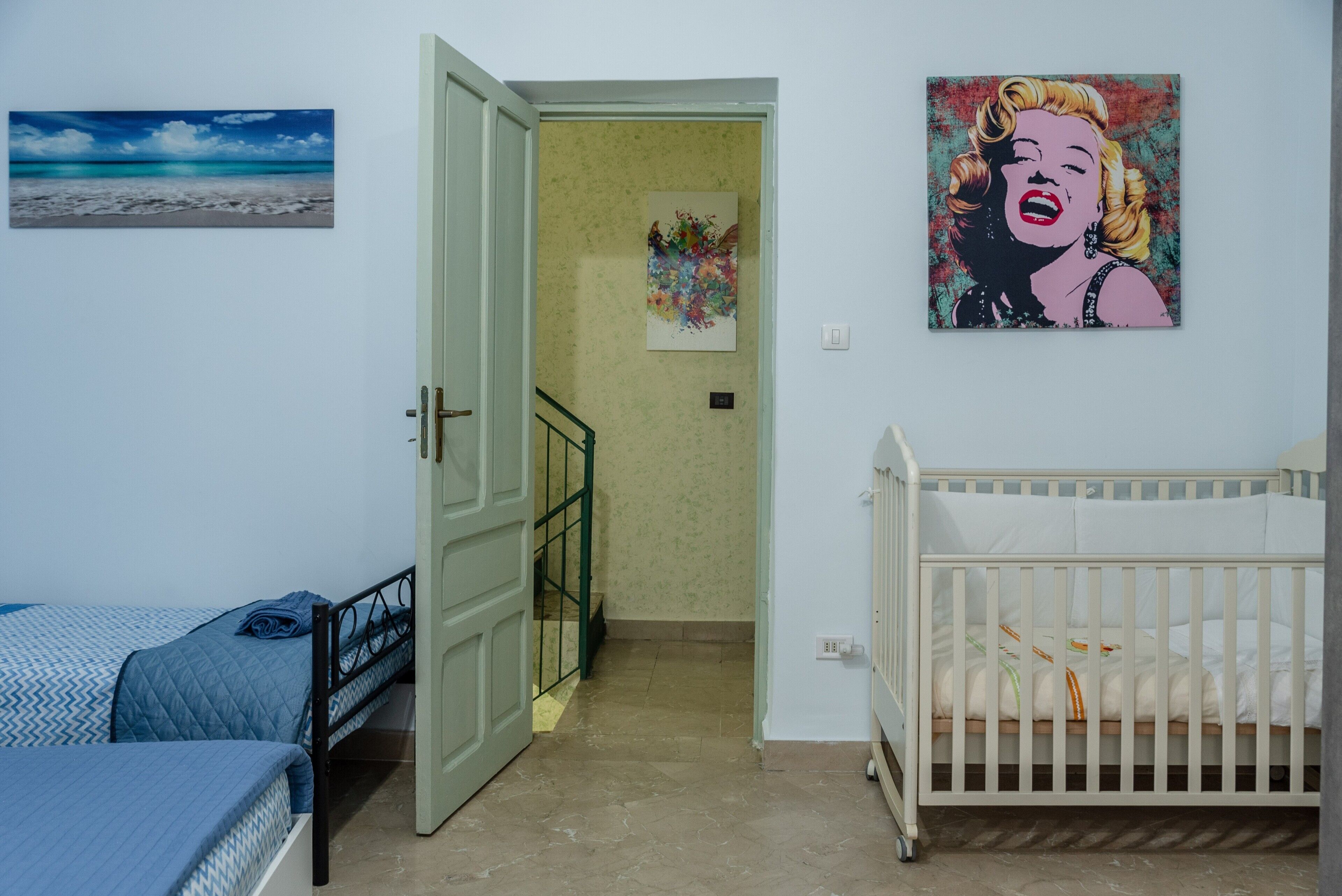 Una stanza con un letto, una culla, una porta che dà su un corridoio e un quadro appeso al muro.