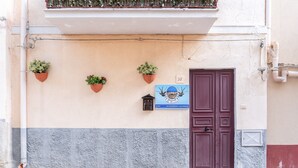 Facciata di un edificio con un portone, tre piante in vaso e un cartello con un numero.
