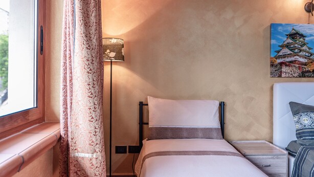 A hotel room with a bed, bedside table, lamp, and a painting of a castle. - Apartment 'Le Rondini' with Wi-Fi and A/C (Siculiana)