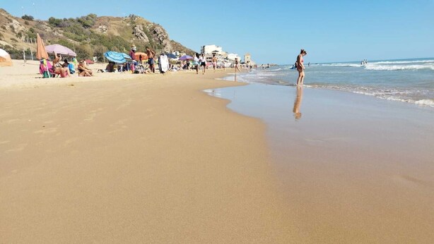 Una spiaggia con persone, ombrelloni e edifici sullo sfondo.