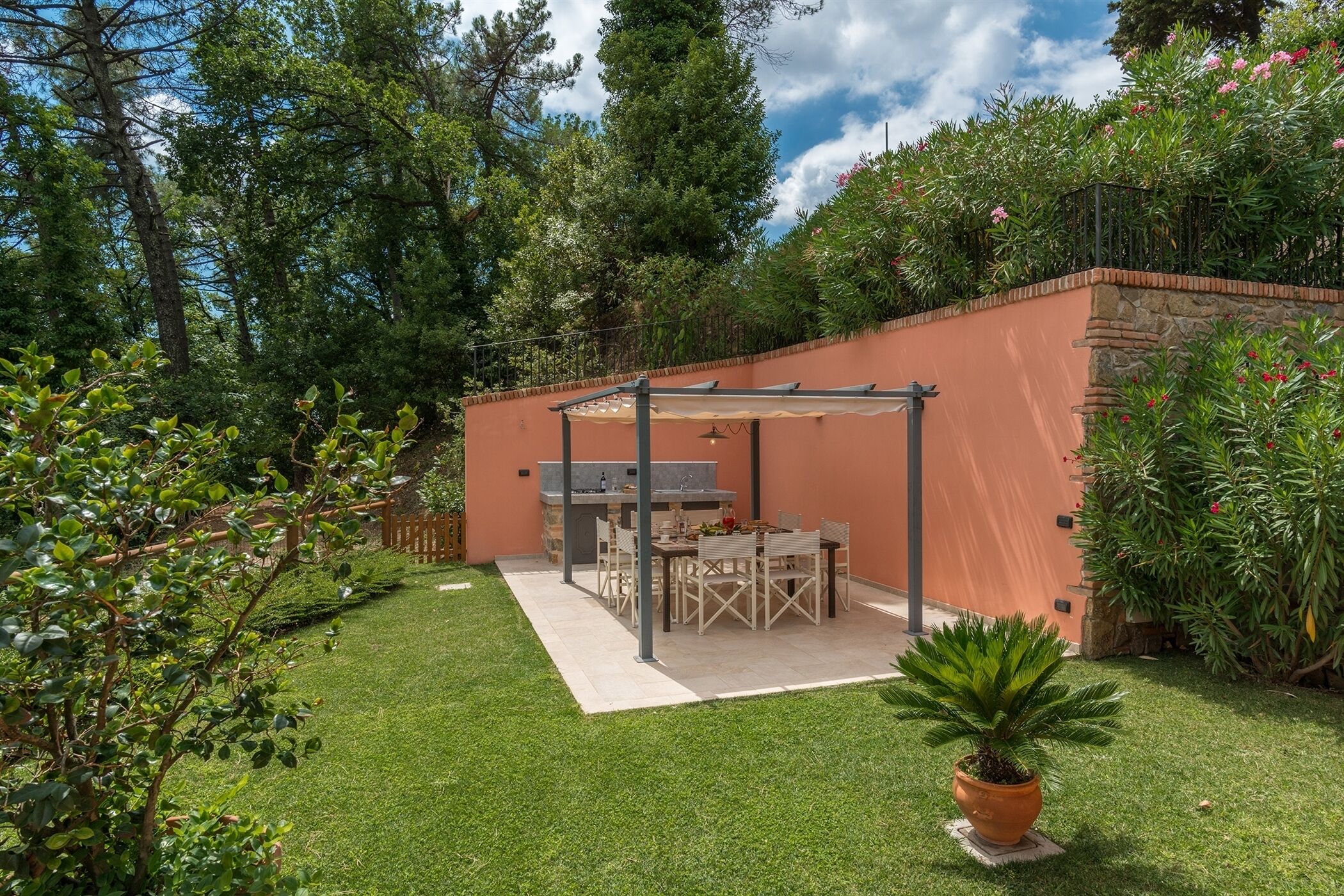A patio area with a table and chairs, surrounded by a stone wall and lush greenery.