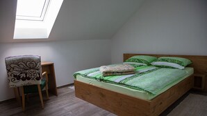 A bedroom with a sloped ceiling, a wooden bed, a green and white patterned bedspread, and a chair with a patterned cushion. - Hocka Koca (Hoce-Slivnica)