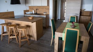 A modern kitchen with wooden cabinetry, a central island with stools, and a dining area with a green upholstered chair and table. - Hocka Koca (Hoce-Slivnica)