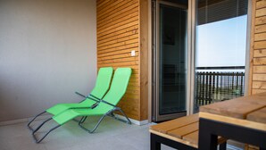 A balcony with two green lounge chairs, a wooden table, and a sliding glass door. - Hocka Koca (Hoce-Slivnica)