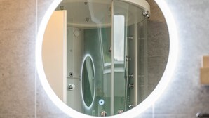 Un miroir rond reflétant l’intérieur d’une salle de bain, notamment une zone de douche et des toilettes.