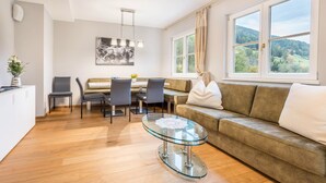 Un salon moderne avec une table basse en verre, des fauteuils gris, un canapé et une table à manger.