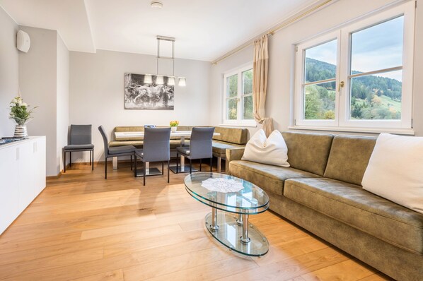 A modern living room with a glass coffee table, grey chairs, a sofa, and a dining table.