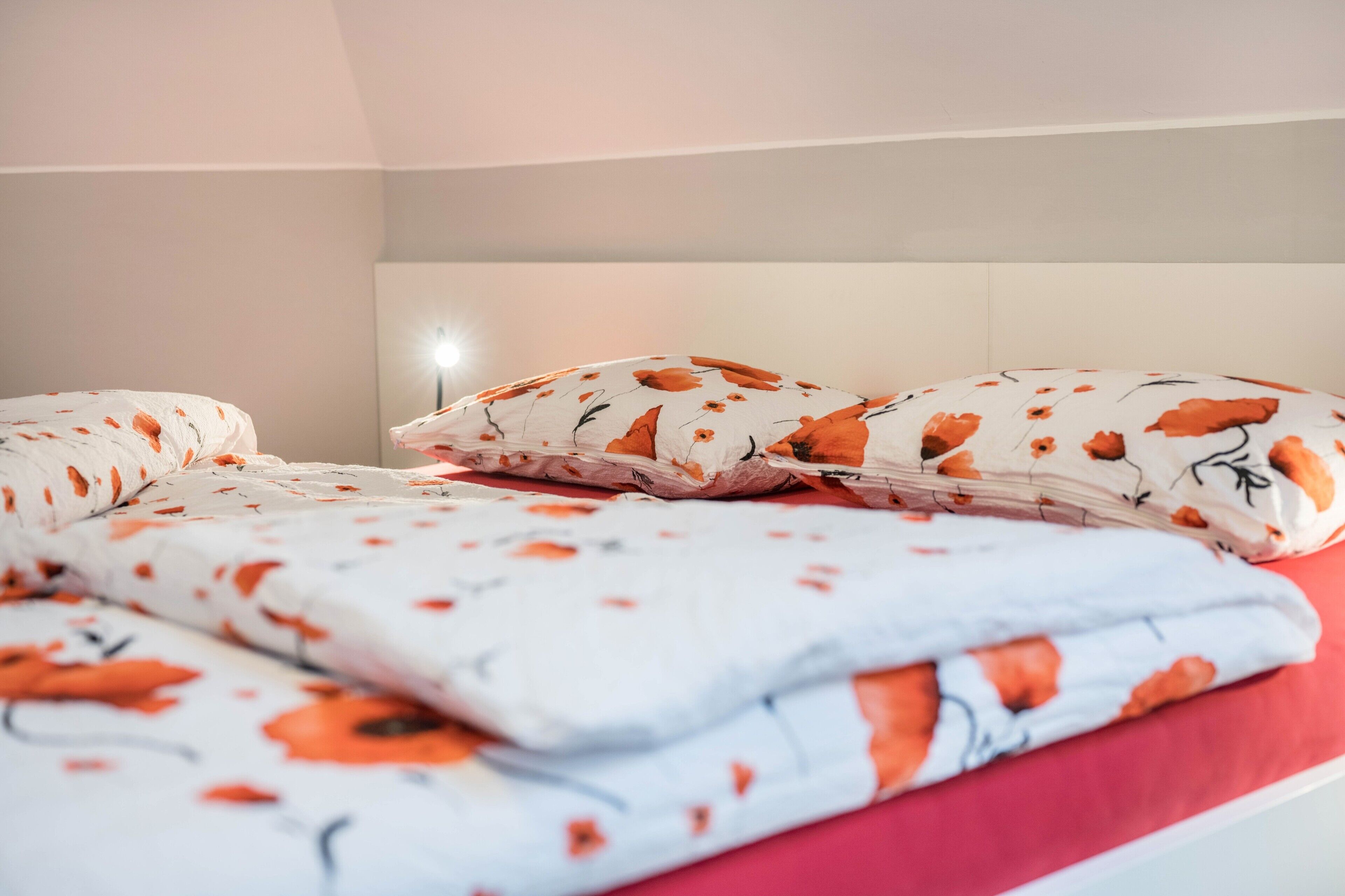 Una cama bien hecha con ropa de cama floral, un cojín rojo decorativo y un cabecero.