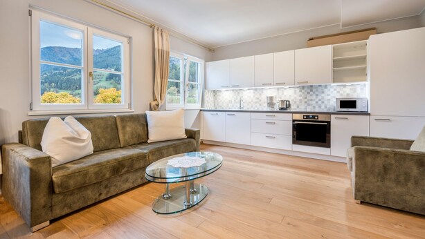 Une cuisine moderne avec des meubles blancs, une table basse en verre et un canapé.
