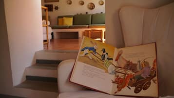 A book open on a chair in a living room with a staircase leading to another room.