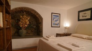 A bedroom with a stone arch, a bed with neatly folded towels, a nightstand with a lamp, and a framed picture on the wall. - Holiday Home 'Casa Annamaria' (Arcola)