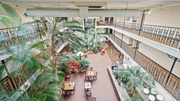 A multi-level atrium with indoor seating, palm trees, and a central staircase. - Coratel Suites 1 King Suite Oversized with Sofa Non-Smoking (Wichita)