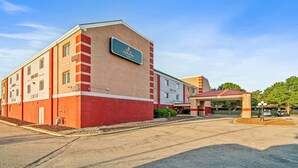 A hotel with a prominent sign, a parking lot, and a building entrance. - Coratel Suites 1 King Suite Oversized with Sofa Non-Smoking (Wichita)