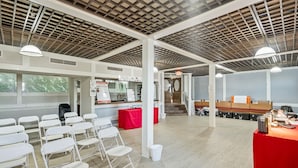 A spacious indoor area with white folding chairs arranged in rows, a red table with items on it, and a staircase in the background. - Coratel Suites 1 King Suite Oversized with Sofa Non-Smoking (Wichita)