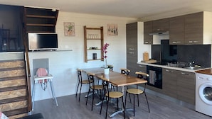 A compact kitchen with a dining area, a washing machine, and a TV mounted on the wall.