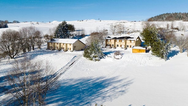 A snow-covered landscape with two buildings, one with a large garage, surrounded by trees and open fields.