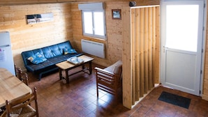 A cozy cabin interior with a wooden floor, a sofa, a dining table, and a staircase.
