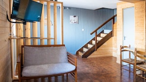 A room with a wooden chair, a television mounted on a wooden structure, a staircase, and a door.