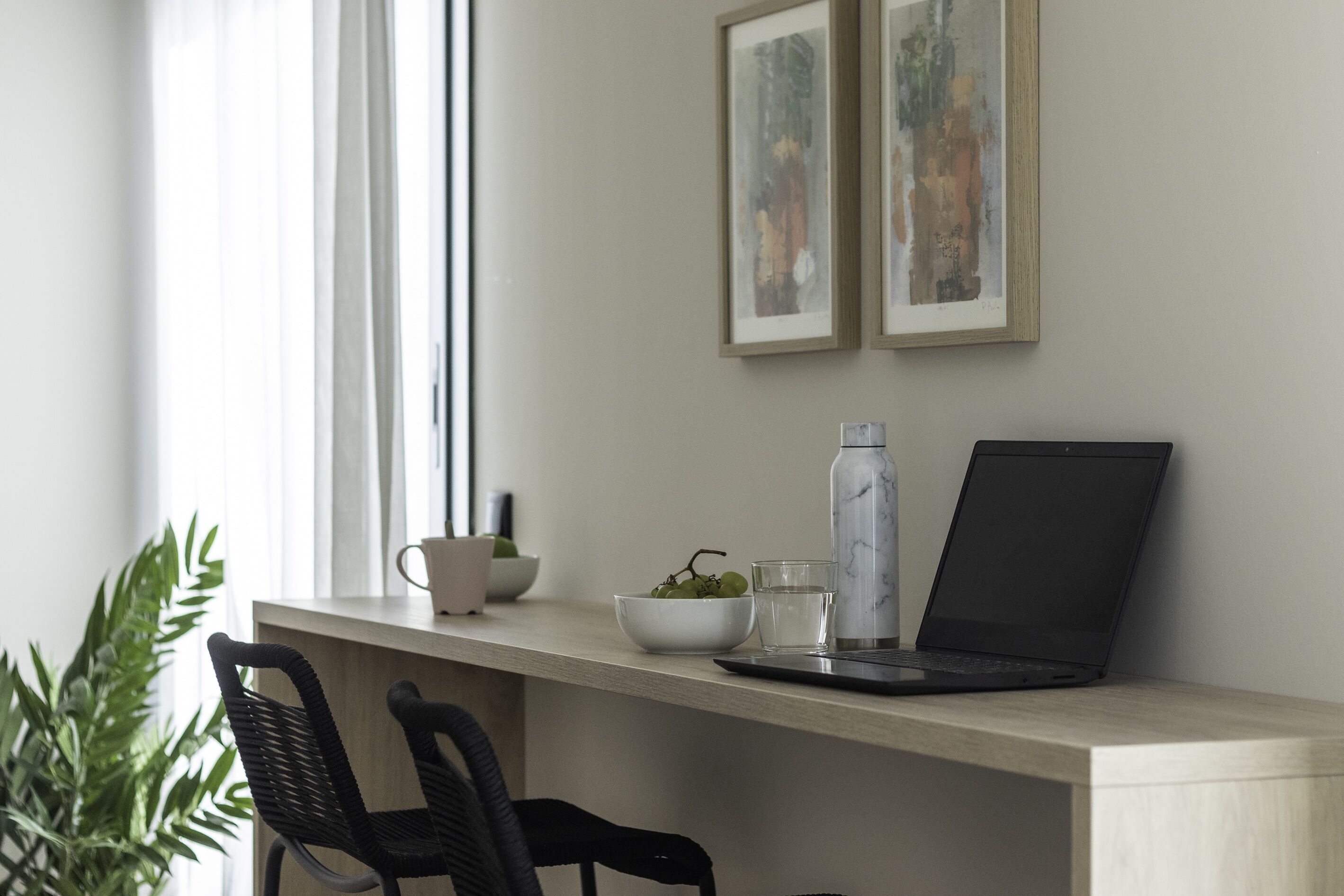 Un espacio de trabajo con una computadora portátil, una botella de agua y un bol de uvas sobre un escritorio.