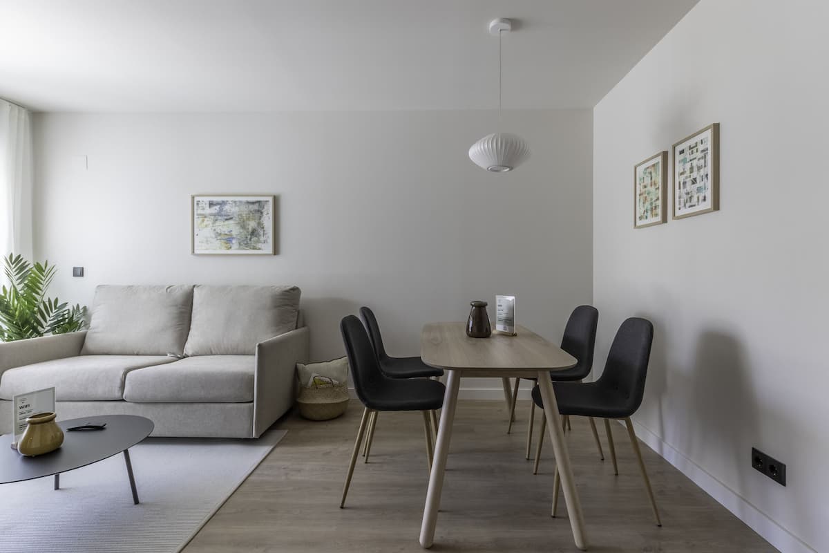 A modern living room with a sofa, a dining table with chairs, a hanging light fixture, and framed artwork on the walls.