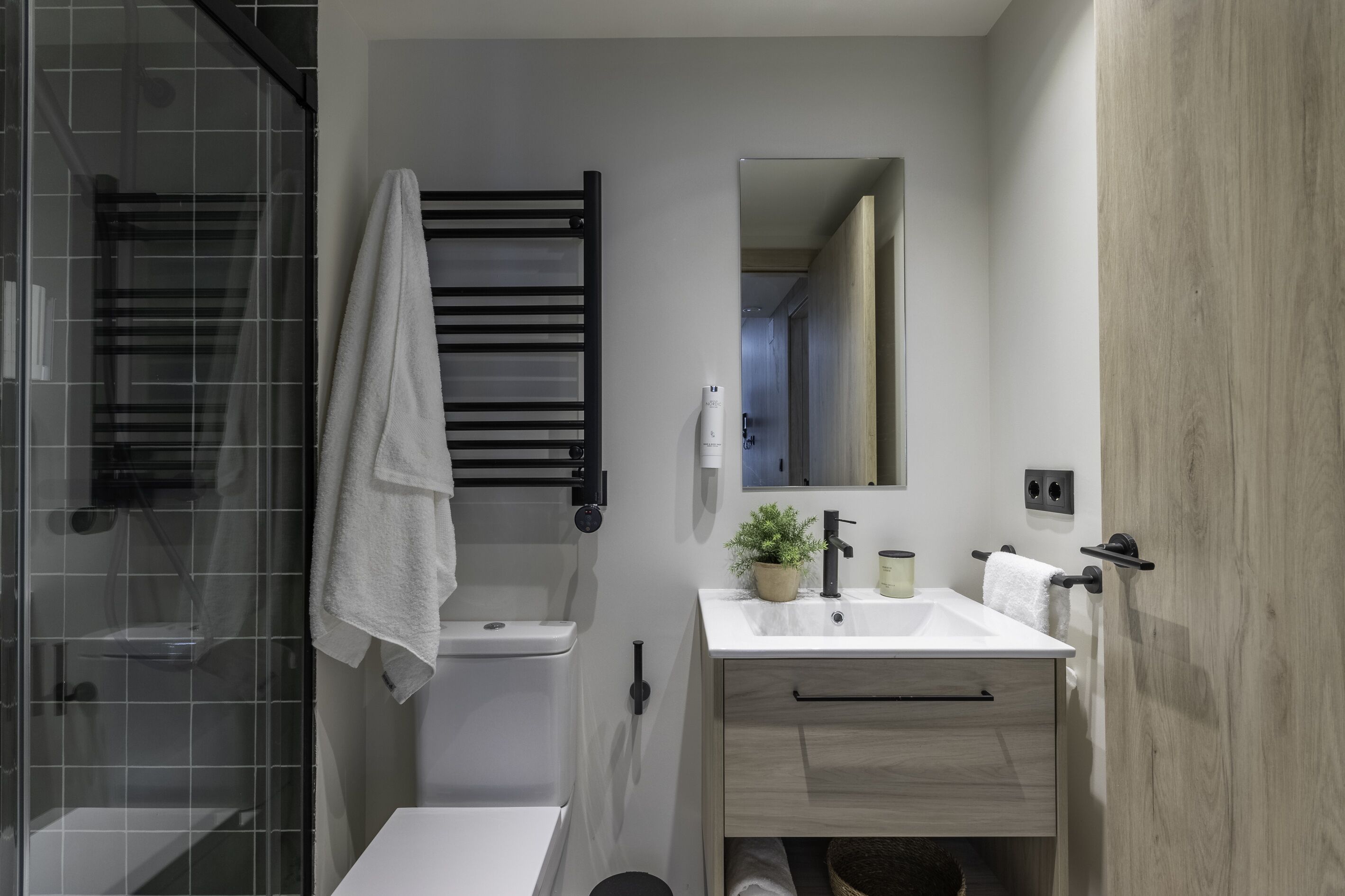 Un baño moderno con cabina de ducha de vidrio, un lavabo blanco, un espejo y un mueble de tocador de madera.