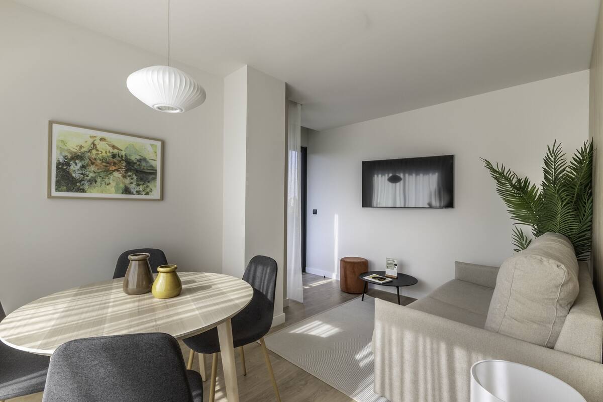 A modern living room with a round dining table, two chairs, a sofa, a coffee table, and a TV mounted on the wall.