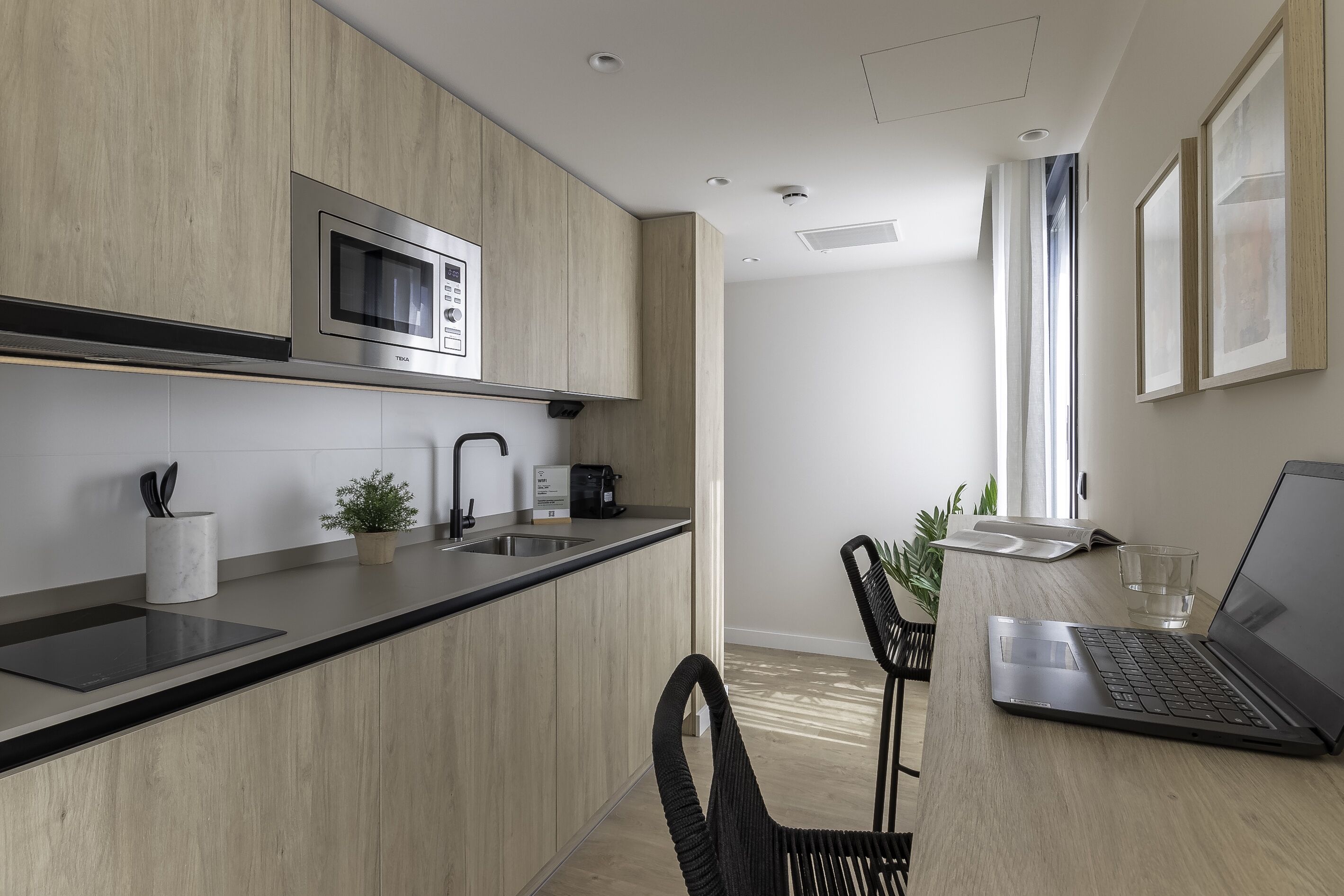 A modern kitchen with a built-in microwave, a coffee machine, and a sink. There is a dining area with a laptop and a glass of water on the table.